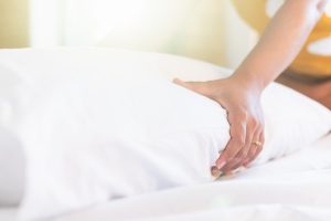 Hand of housekeeper set up white pillow on the bed sheet in hotel room at morning time with sunlight from windows