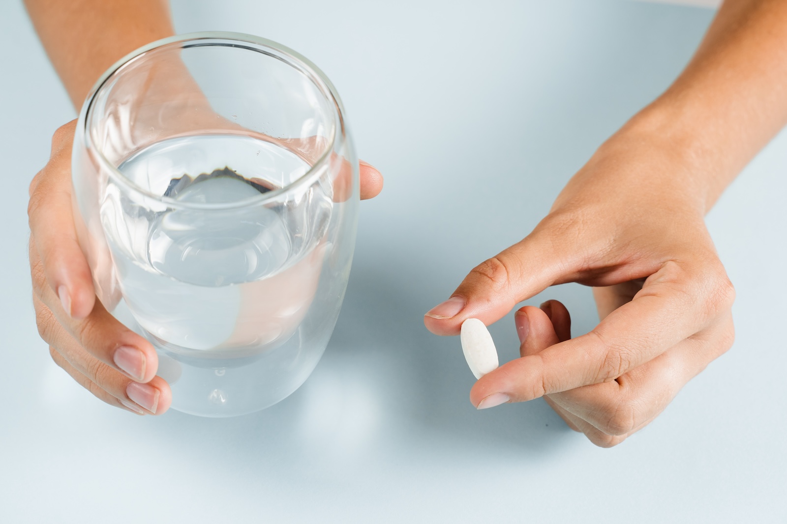 White pill of dietary biologically active supplements and glass of water for daily tablets intake on blue background.