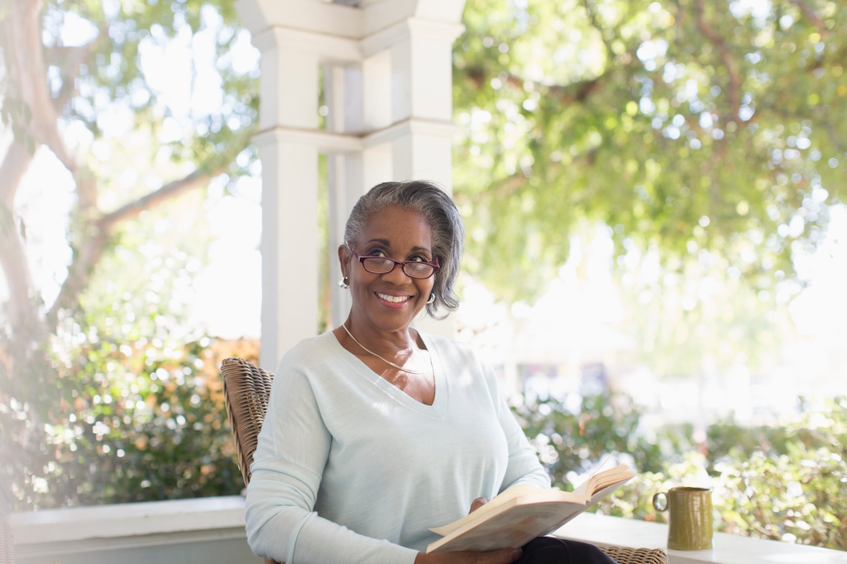 Portrait happy senior woman reading book on sunny porch