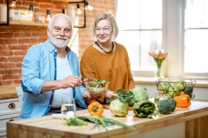 Cheerful senior couple eating salad standing together with healthy food on the kitchen at home. Concept of healthy nutrition in older age